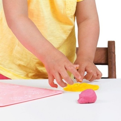 Criança a modelar massa amarela com massa rosa ao lado.