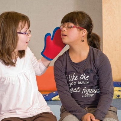 Duas raparigas sentadas no chão com roupa casual, uma usando luva vermelha de brincar.