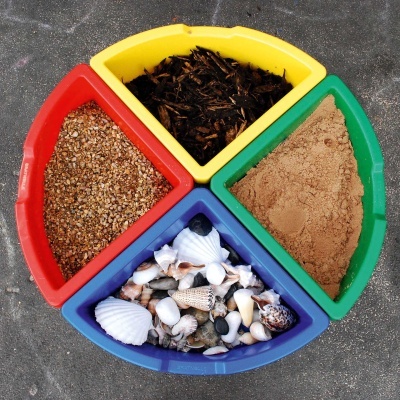 Recipientes coloridos com sementes, conchas, madeira picada e pó castanho