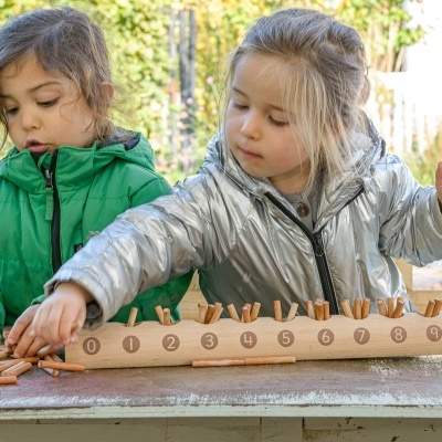 Duas crianças a jogar jogo educativo de números em madeira numa mesa exterior