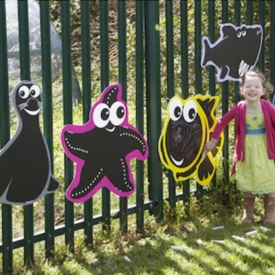 Painéis decorativos de animais marinhos coloridos numa grade ao ar livre com uma criança ao lado