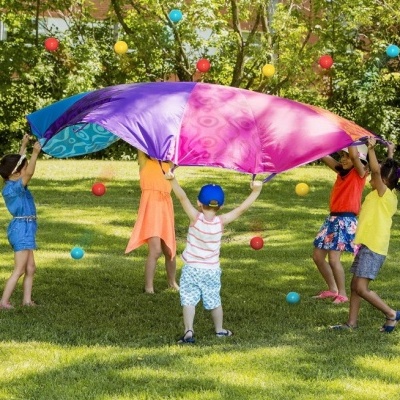 Crianças brincando com tecido colorido ao ar livre com bolas coloridas ao redor