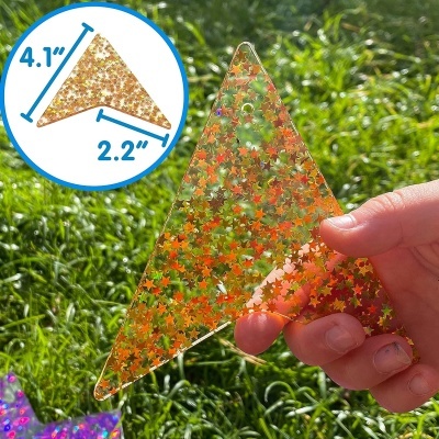 Triângulo de acrílico transparente com glitter colorido em forma de estrelas, segurado à luz do sol com relva ao fundo