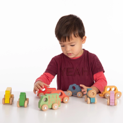 Criança a brincar com carros de madeira coloridos sobre mesa branca