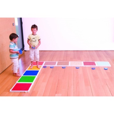 Dois meninos descalços brincando em tapetes coloridos posicionados em L no chão de madeira claro dentro de uma casa