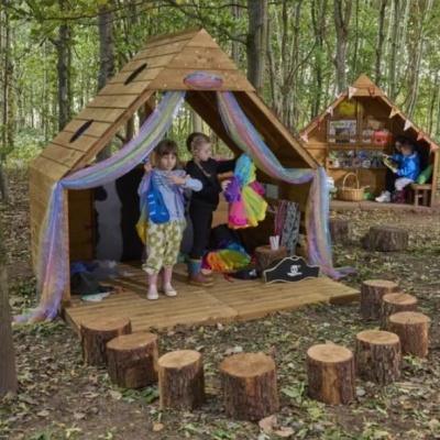 Casas de madeira para brincar com cortinas coloridas e troncos para sentar em ambiente natural