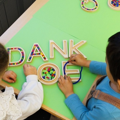 Crianças a manipular letras de madeira e peças coloridas numa mesa verde