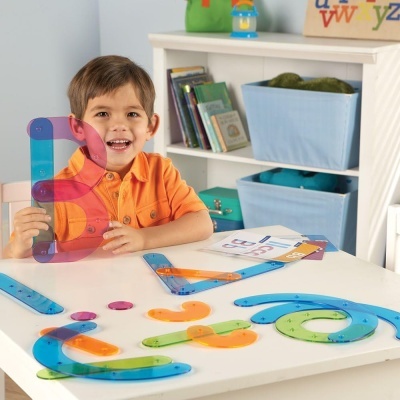 Menino alegre com réguas coloridas e estante com caixas azuis e livros ao fundo.