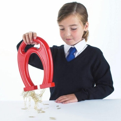 Menina com íman vermelho a atrair clips de papel sobre mesa branca