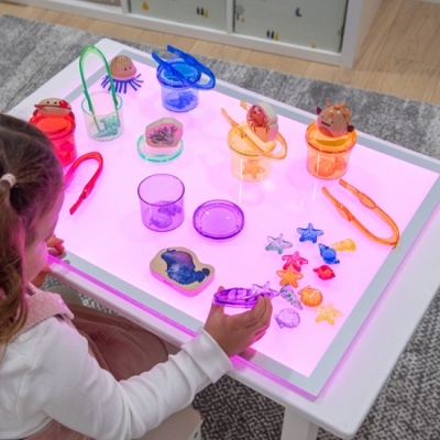 Mesa iluminada rosa com brinquedos plásticos coloridos e criança brincando