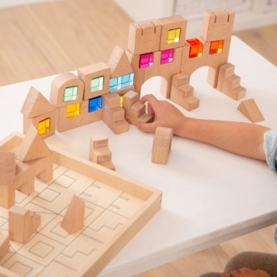 Brinquedo de blocos de madeira com janelas coloridas e criança a brincar numa mesa branca