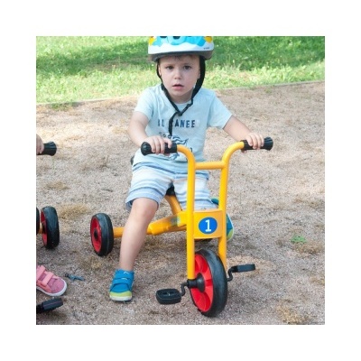 Criança num triciclo amarelo com capacete azul num parque