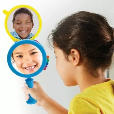 Criança segurando espelhos redondos azul e amarelo refletindo rostos sorridentes de crianças.