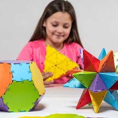 Brinquedo de construção colorido com formas geométricas e menina ao fundo com t-shirt rosa