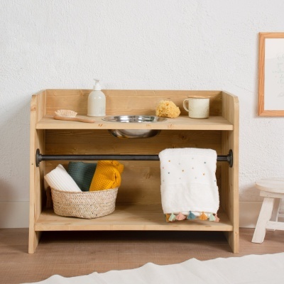 Móvel em madeira clara com prateleira superior com acessórios de higiene e toalhas penduradas