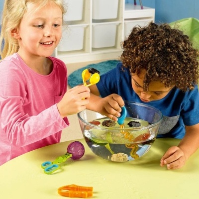 Crianças a brincar com brinquedos de mergulho em taça de vidro com água numa mesa amarela