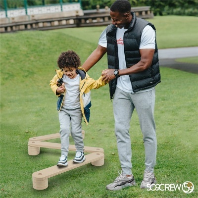 Homem a ajudar criança a andar numa estrutura de equilíbrio em madeira num relvado