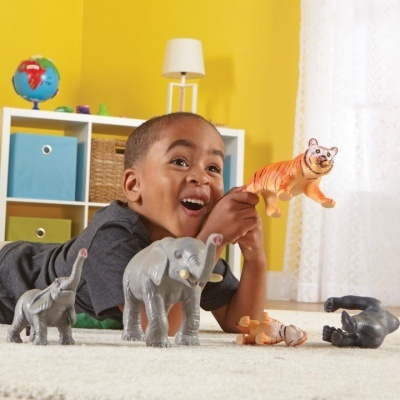 Menino brinca com figuras de animais de plástico numa sala amarela.