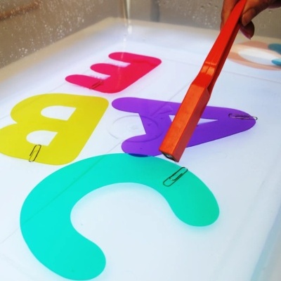 Letras coloridas em plástico com clips dentro de um recipiente com água e vareta magnética vermelha na mão