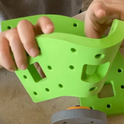 Peças verdes de plástico com furos e formas geométricas nas mãos de uma criança.