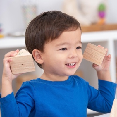 Menino com camisa azul segurando blocos de madeira quadrados num ambiente interior