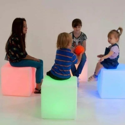 Crianças sentadas em cubos iluminados coloridos em fundo branco