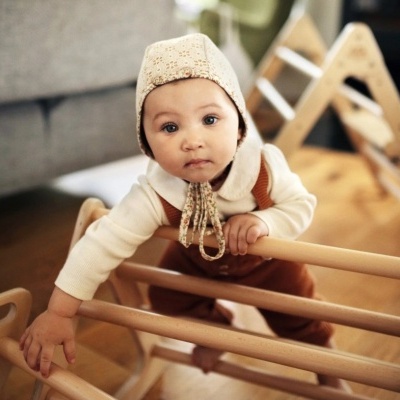 Bebé com roupa creme e castanha junto a estrutura de madeira clara em quarto doméstico
