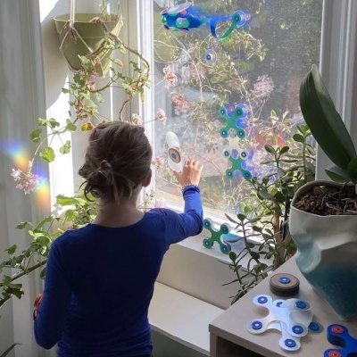 Criança com camisola azul junto a janela com plantas e brinquedos azuis e brancos montáveis