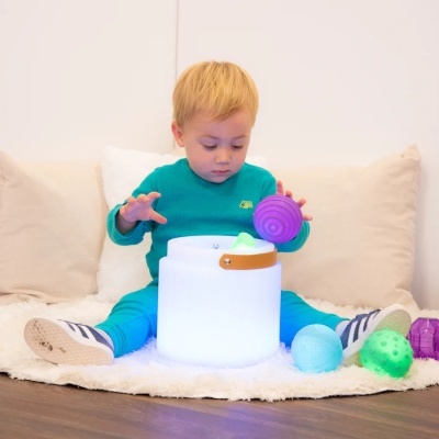 Criança sentada a brincar com bolas coloridas num tapete com almofadas