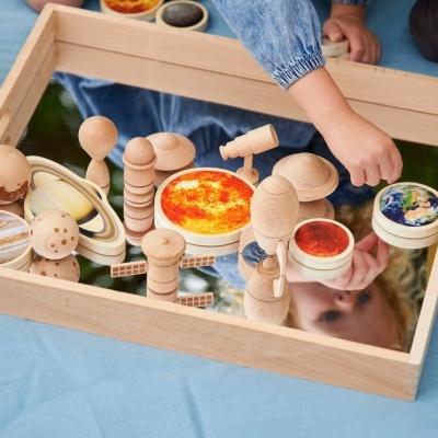 Conjunto de planetas em madeira sobre espelho com moldura de madeira e criança a tocar nas peças