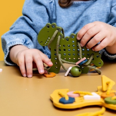 Criança a jogar com brinquedo educativo dinossauro verde em madeira com fios e peças coloridas