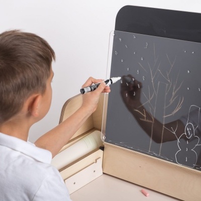 Menino a desenhar numa placa de acrílico preta com suporte de madeira