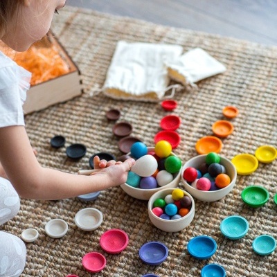 Criança a brincar com bolas e tampas coloridas em tapete bege
