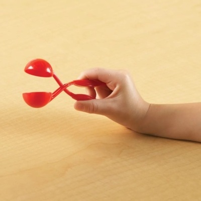 Mão de criança segurando acessório plástico vermelho sobre superfície de madeira