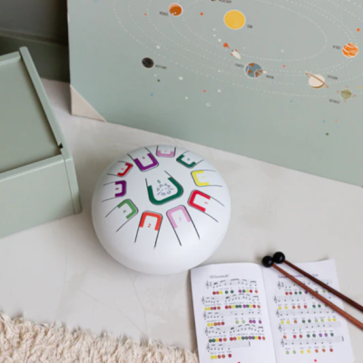 Tambor de língua em aço branco com notas coloridas e partitura musical com baquetas