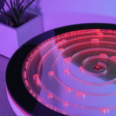 Placa redonda de acrílico iluminada com luz vermelha junto a vaso branco e planta