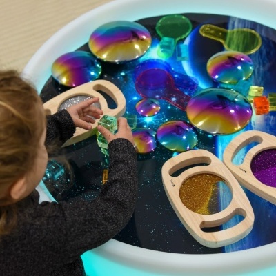 Brinquedo sensorial com peças coloridas transparentes e madeira numa mesa iluminada