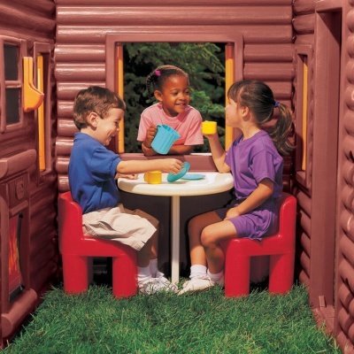 Crianças brincando de chá em casinha de brincar com cadeiras e mesa de plástico