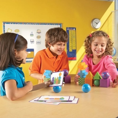 Três crianças a brincar com blocos de construção coloridos numa sala amarela