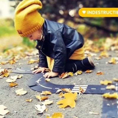 Criança a brincar com tapete de estrada no chão coberto de folhas de outono