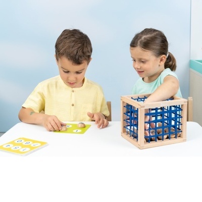 Duas crianças brincam com cartas de números e uma gaiola de madeira azul numa mesa branca