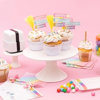 Cupcakes com decoração de aniversário em suporte branco e enfeites coloridos