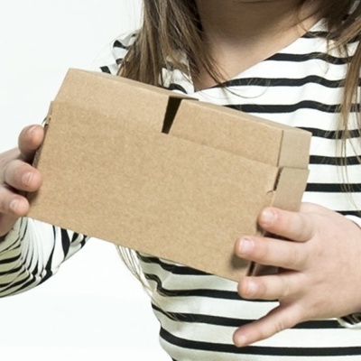 Criança segurando caixa de cartão castanho com mãos em camisa de riscas pretas e brancas