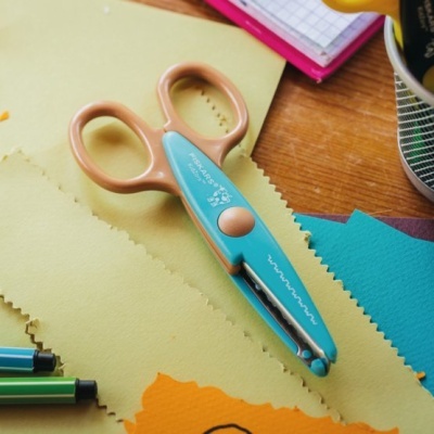 Tesoura de cortiça azul e bege sobre folhas de papel coloridas cortadas com padrão ondulado