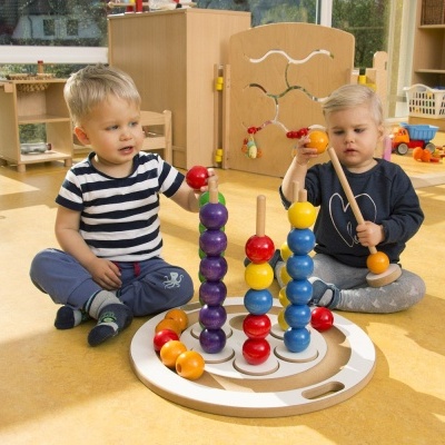Dois bebés sentados a brincar com brinquedo de bolas empilháveis coloridas em sala clara