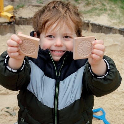 Criança com casaco preto e cinza segura moldes quadrados de areia com padrão floral