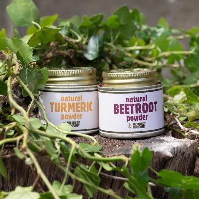 Frascos de pó natural de curcuma e beterraba sobre tronco com folhas verdes