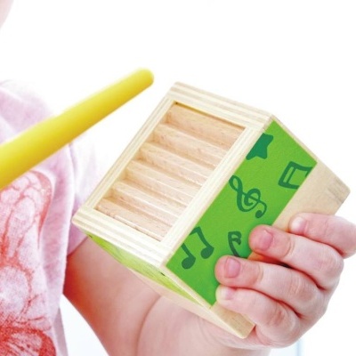 Criança com caixa de instrumentos em madeira verde com notas musicais e baqueta amarela