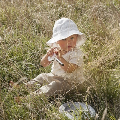 Criança sentada na relva com chapéu branco e roupa clara