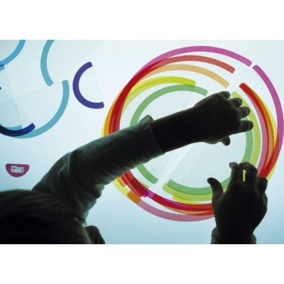 Criança a tocar numa tela interativa com padrões coloridos circulares